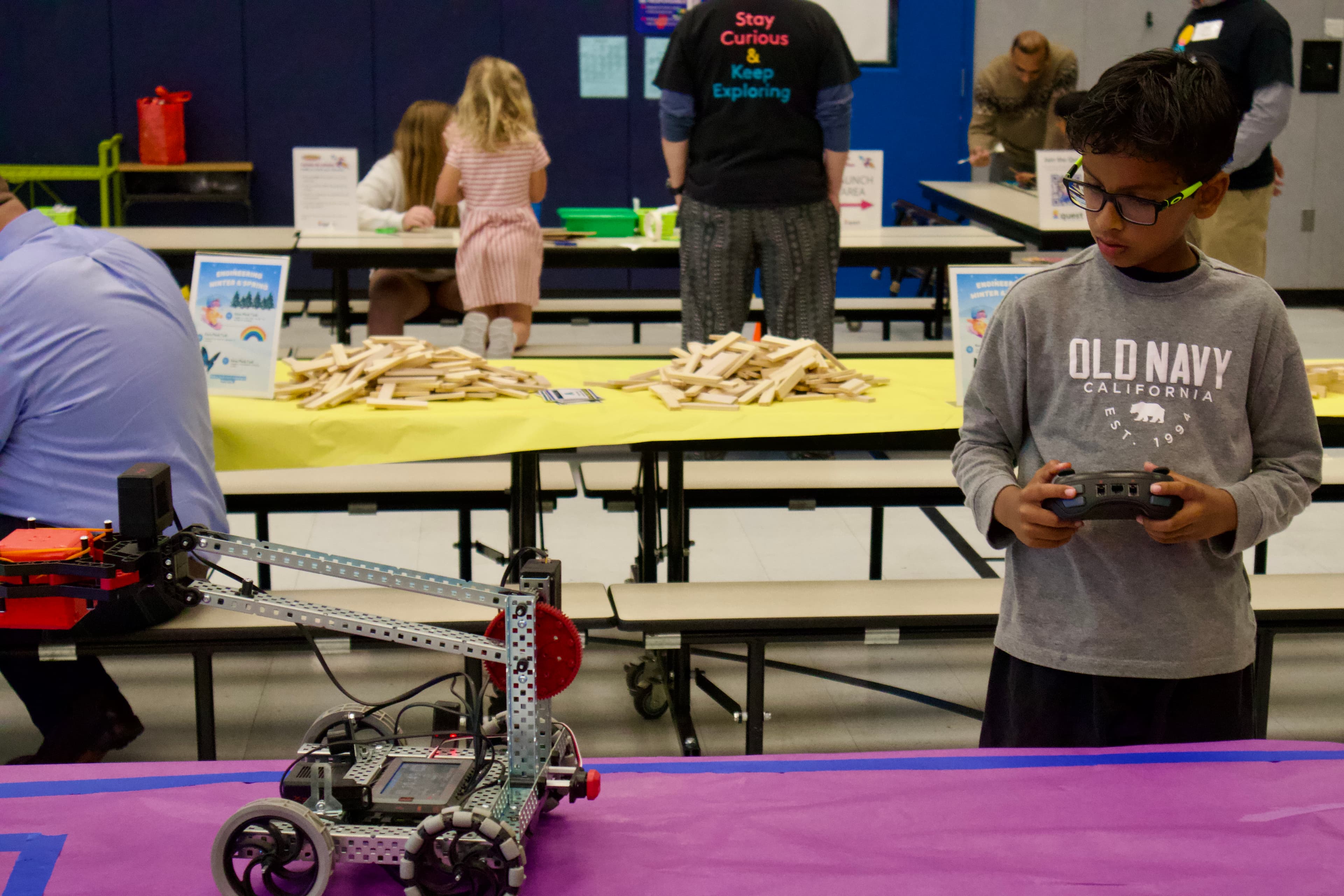 A young participant holds a controller beside a VEX robot.